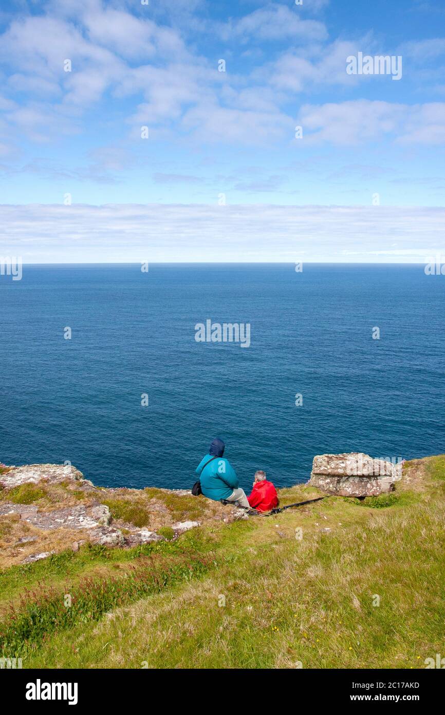 Deux touristes, vêtus de vêtements imperméables, s'assoient sur une falaise en regardant l'océan Atlantique. Île de Handa, Sutherland, Highlands écossais Royaume-Uni Banque D'Images