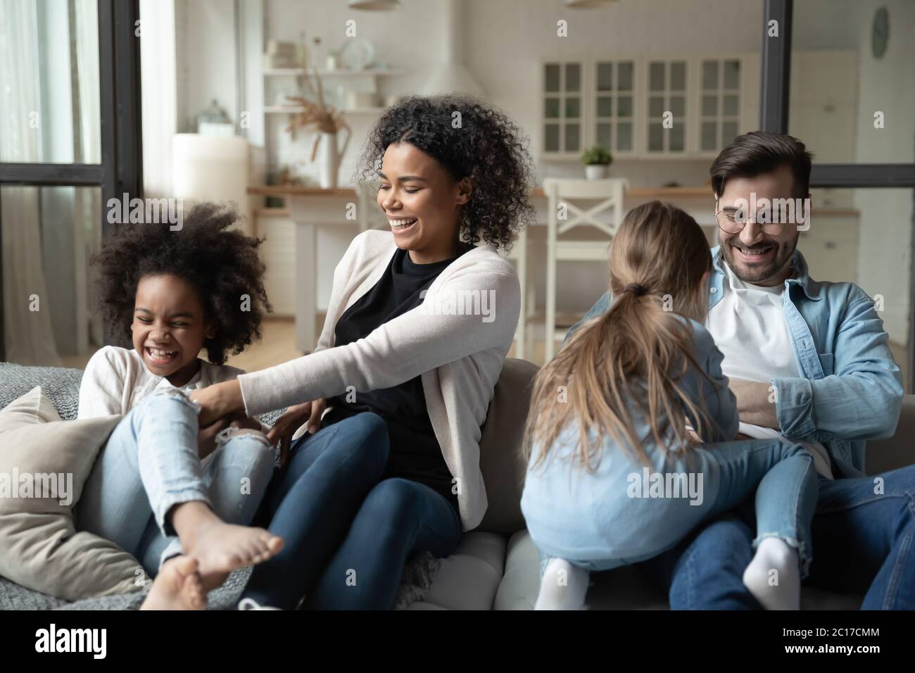 Parents multiraciaux chatouillant les petites filles famille s'amusant à la maison Banque D'Images