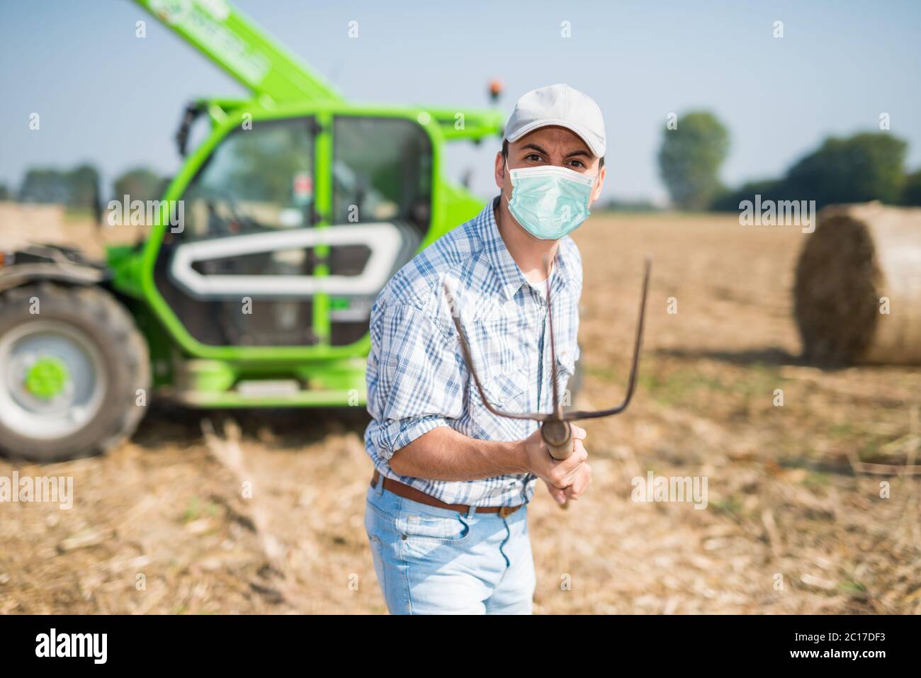 Un fermier en colère masqué pointe sa fourche, son coronavirus et son concept de pandémie Banque D'Images