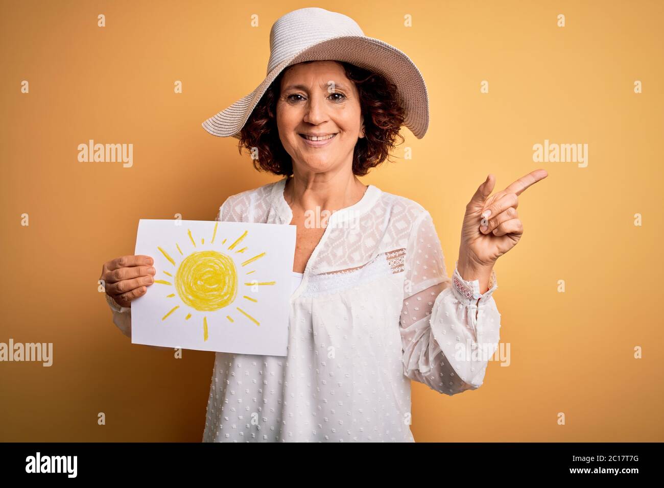 Femme maurique d'âge moyen en vacances tenant bunner avec image de soleil sur fond jaune très heureux pointant avec la main et le doigt sur le côté Banque D'Images