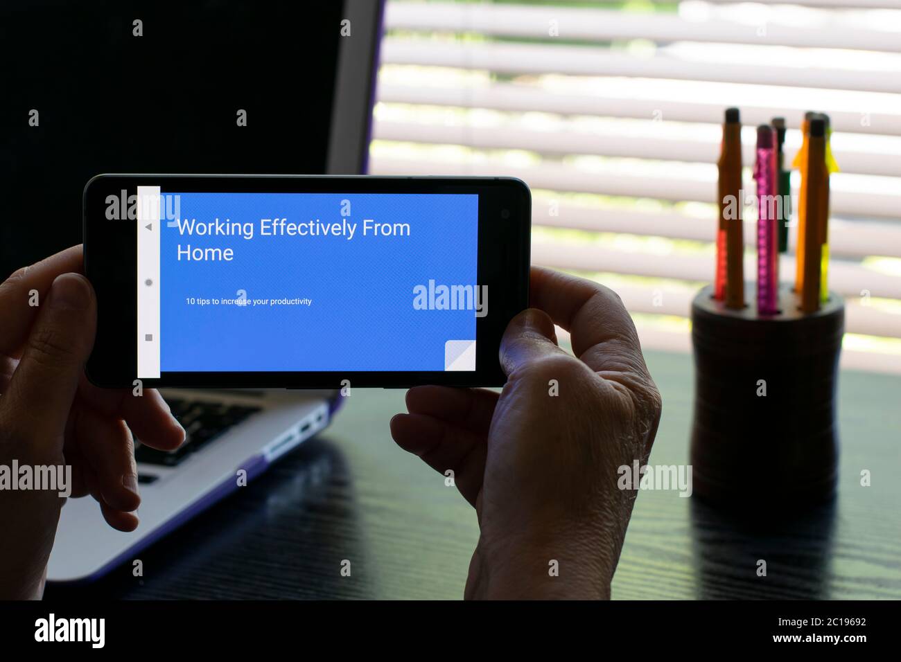 Personne lisant la présentation de diapositives google sur un téléphone mobile android dans un bureau à domicile avec un ordinateur portable en arrière-plan. Texte fonctionnant efficacement à partir de la maison Banque D'Images