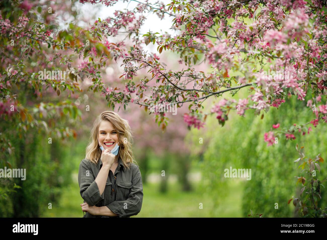 Jeune femme en masque médical sur fond d'arbres en fleurs dans le parc l'après-midi. Banque D'Images