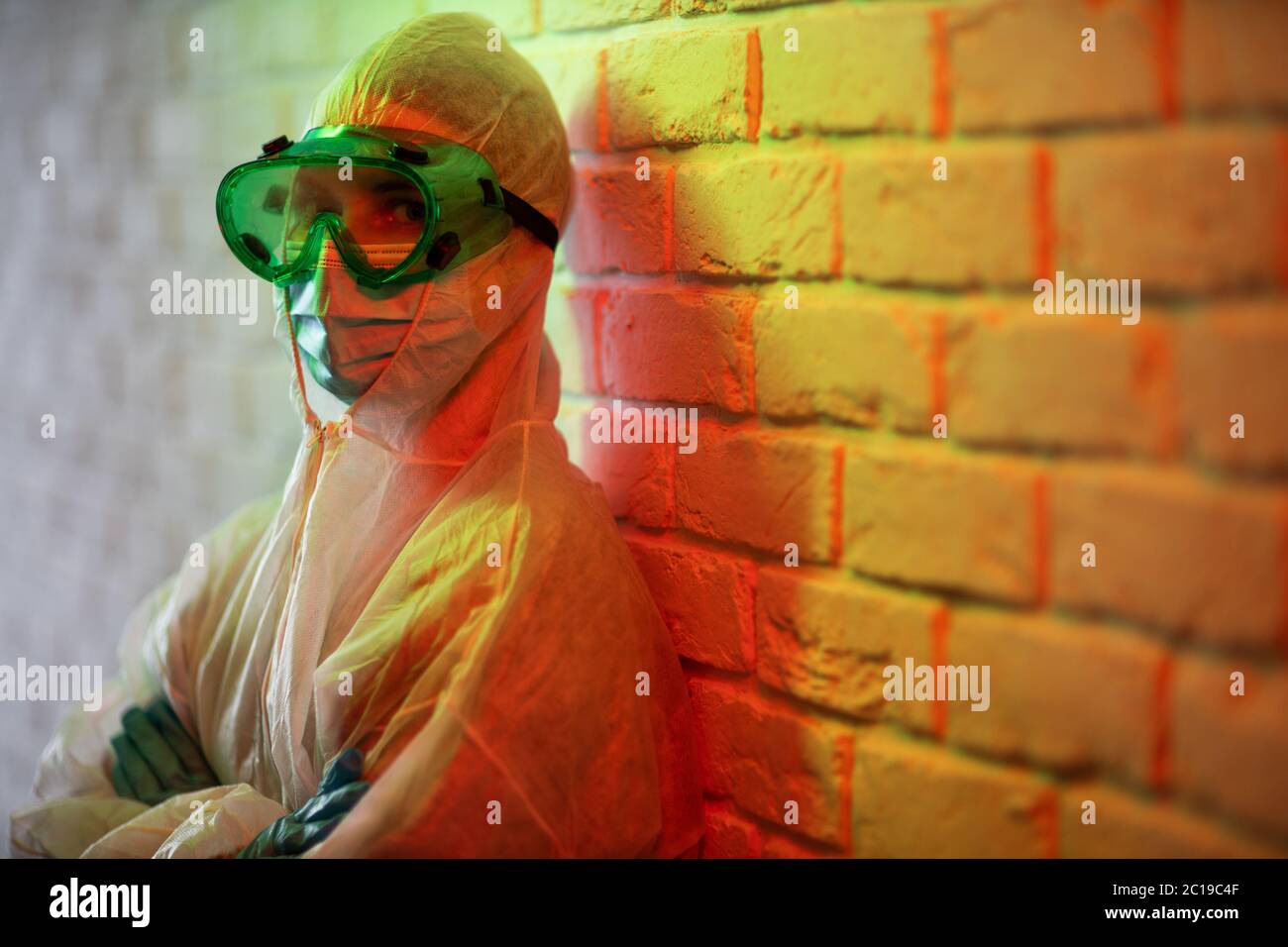 Jeune médecin en costume de protection et lunettes sur fond de mur de briques dans la zone rouge Banque D'Images