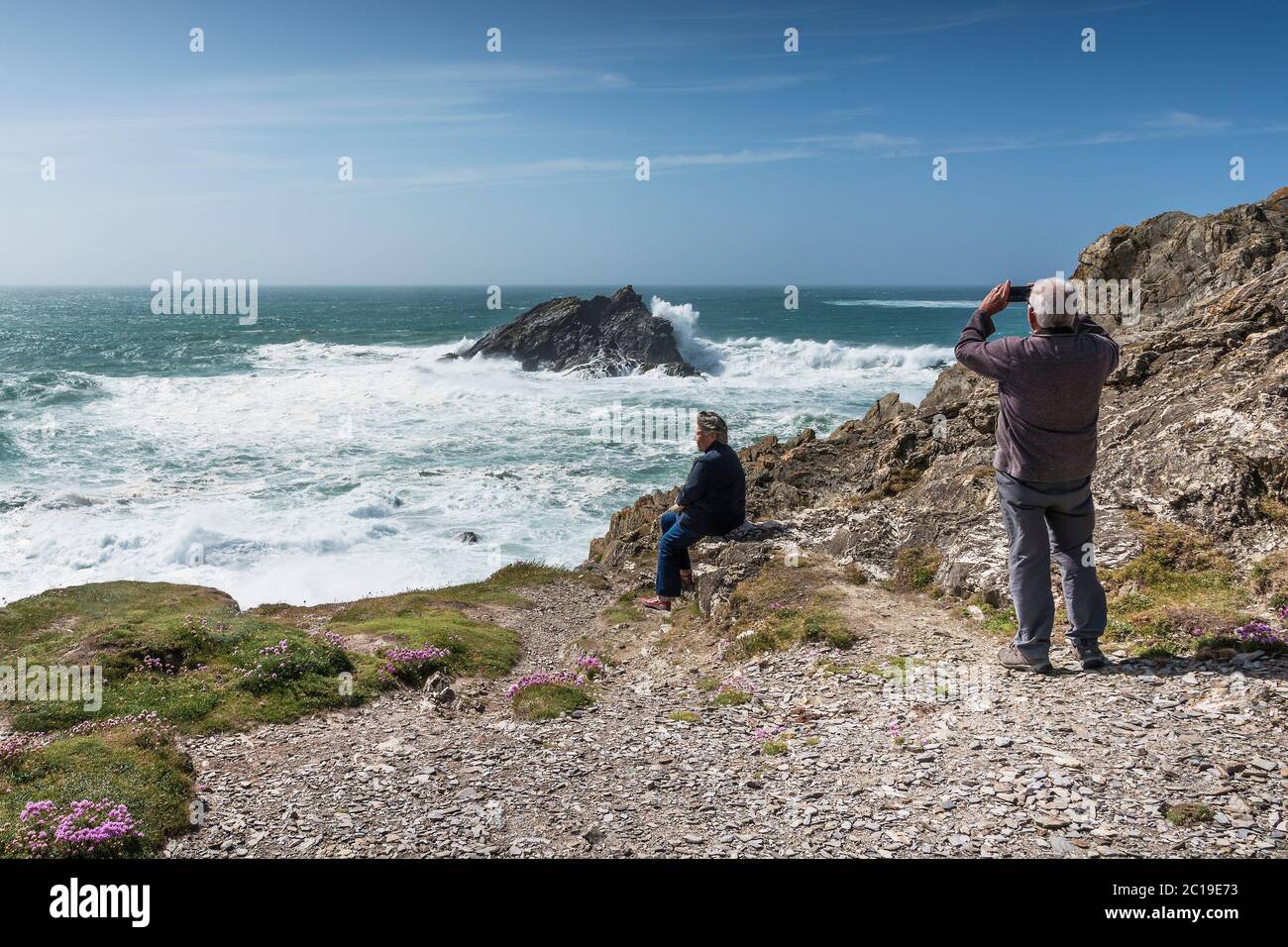 Les touristes apprécient le temps de vent sauvage et utilisent un smartphone pour photographier les vagues qui se brisent au-dessus de Goose Rock au large de la côte de Pentire point East, au nord-est du pays Banque D'Images