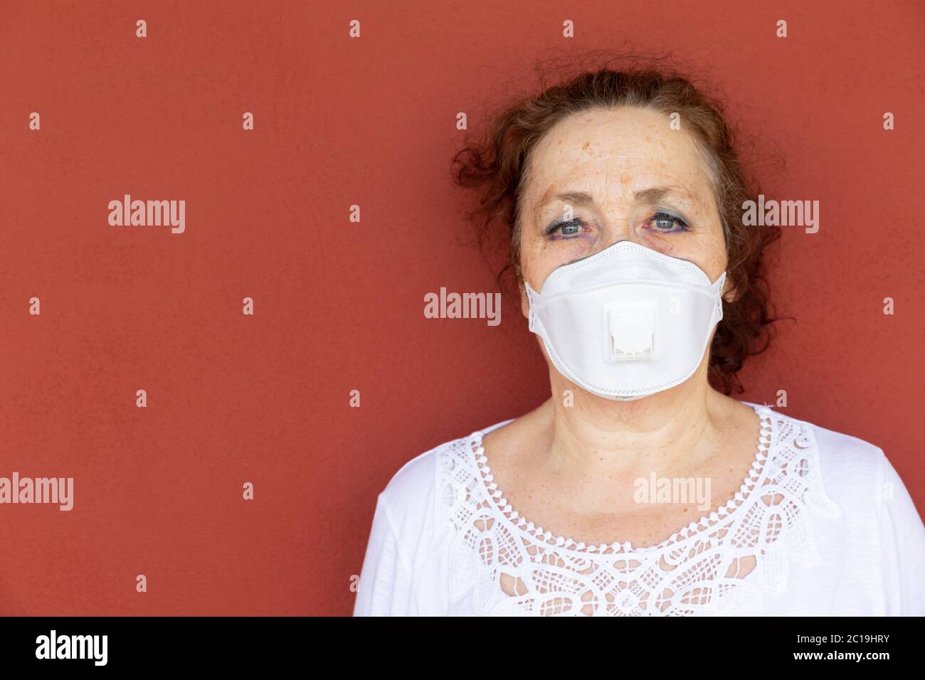 Portrait de la vieille femme avec masque protecteur sur le mur rouge. Confinement par coronavirus. Concept Covid-19. Banque D'Images