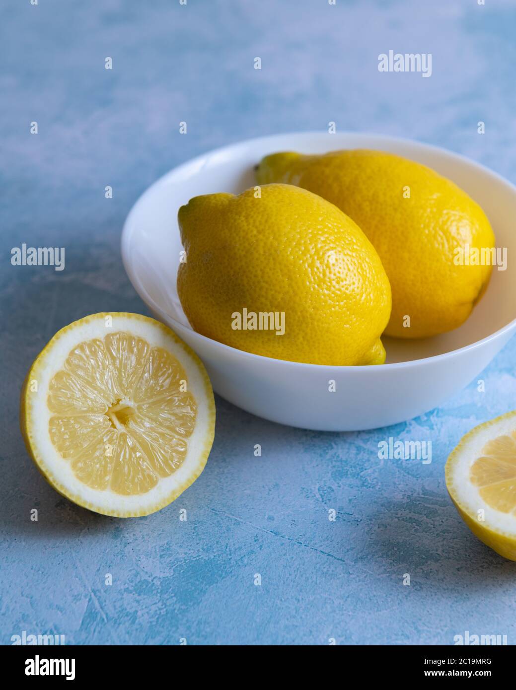 Citrons entiers dans un bol blanc avec des tranches de citron sur fond bleu texturé Banque D'Images