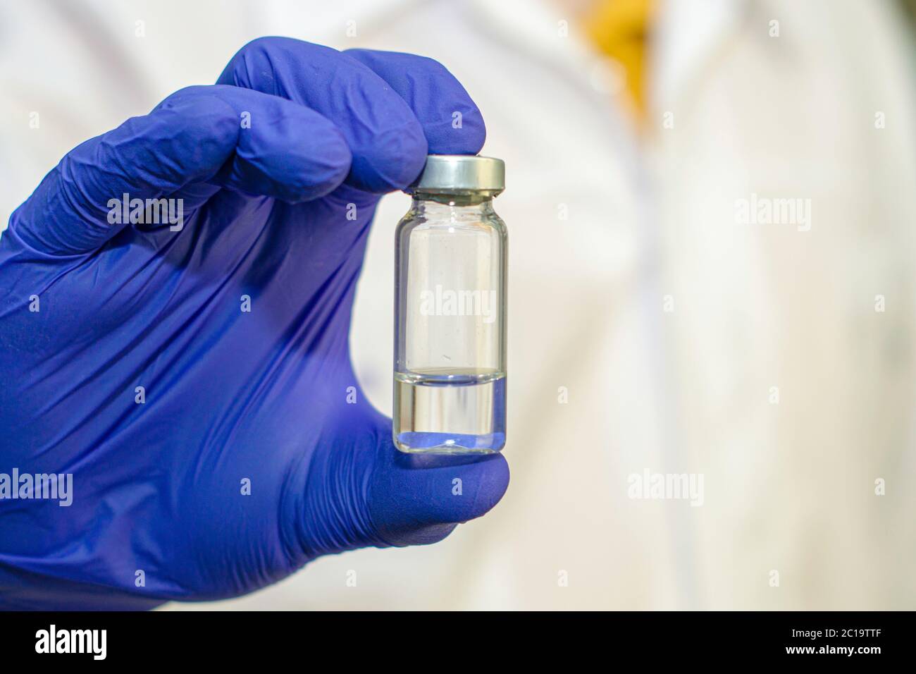 un flacon avec un vaccin dans la main d'un médecin dans sa main bleu gant de protection chirurgical le médecin dans le fond en flou. Banque D'Images