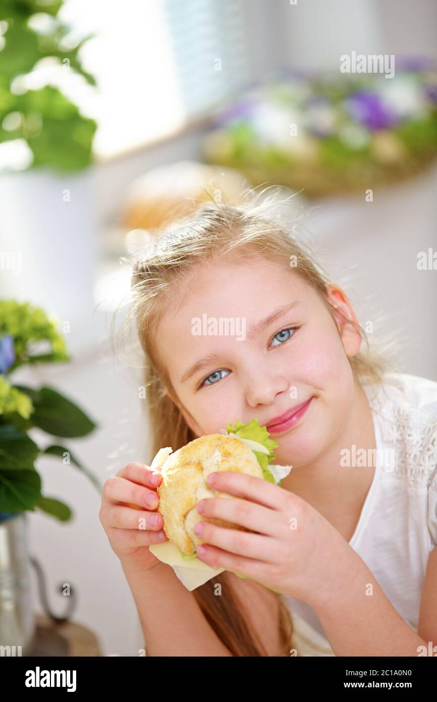 Un enfant heureux prenant le petit déjeuner dans la cuisine avec un sandwich Banque D'Images