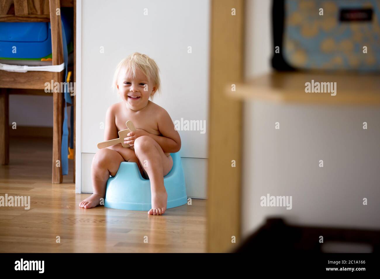 Petit garçon, assis sur un pot, jouant avec un jouet en bois à la maison Banque D'Images