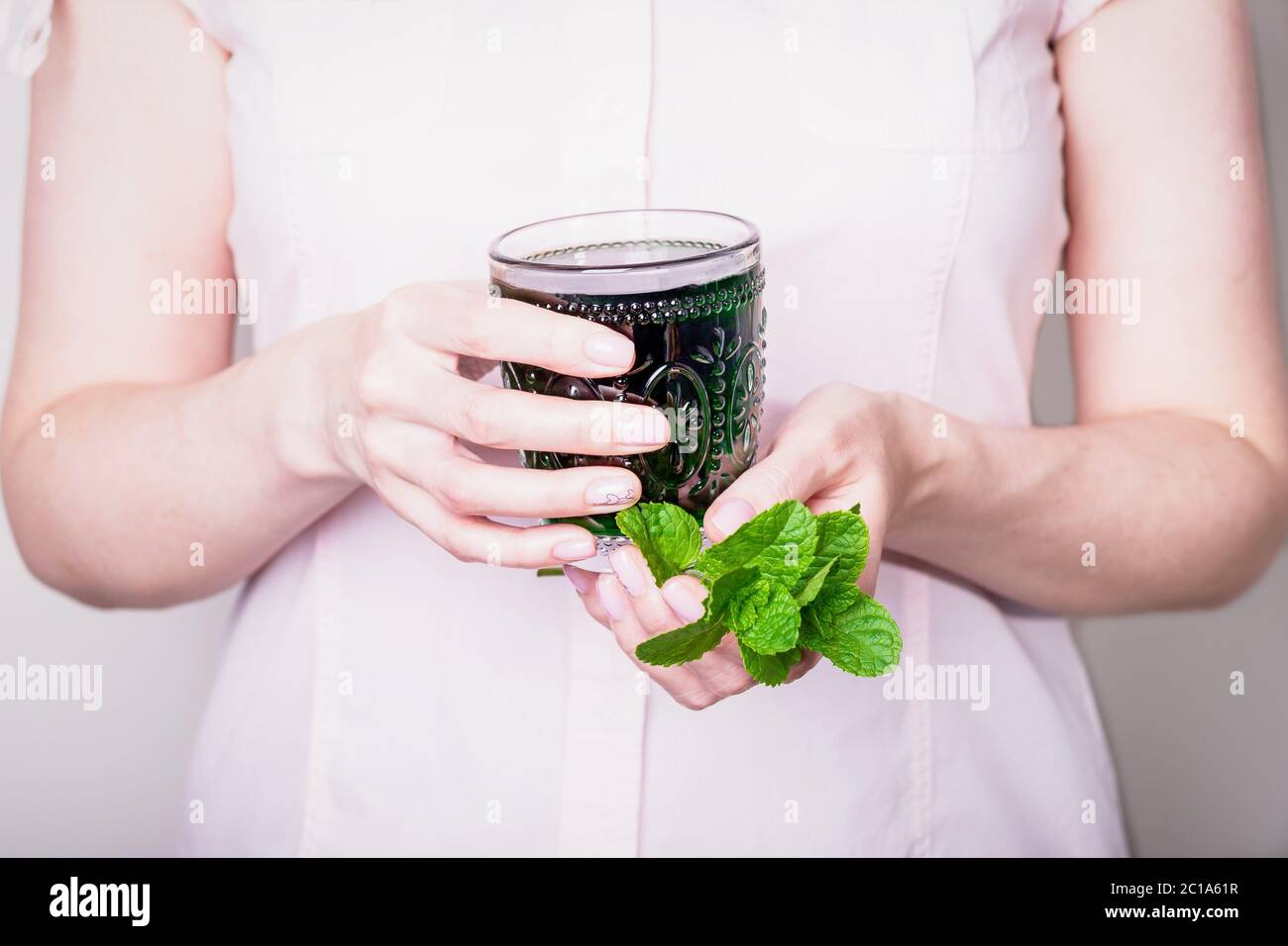 Main femelle tenant un verre de chlorophylle vert avec des feuilles de menthe sur un fond rose clair Banque D'Images