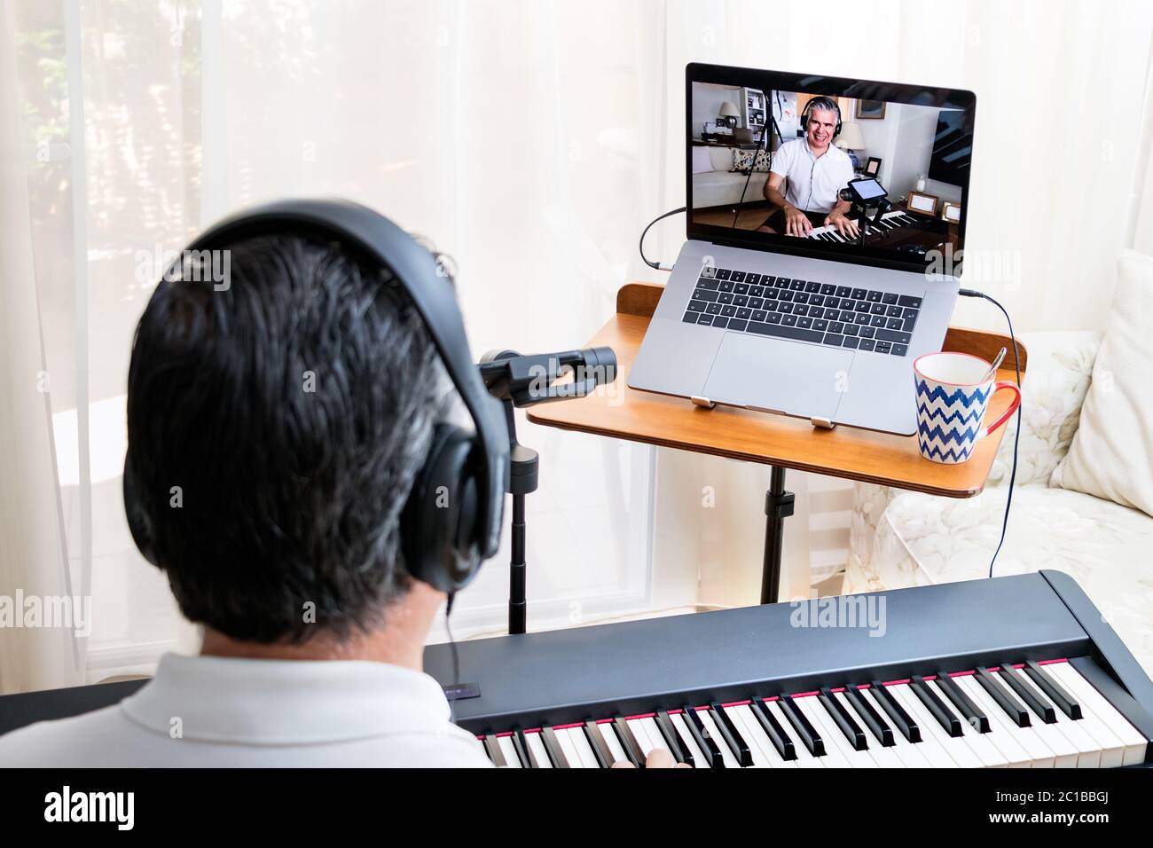 Professeur de piano masculin donnant des leçons de piano en ligne à la maison à l'aide d'un ordinateur portable. Banque D'Images