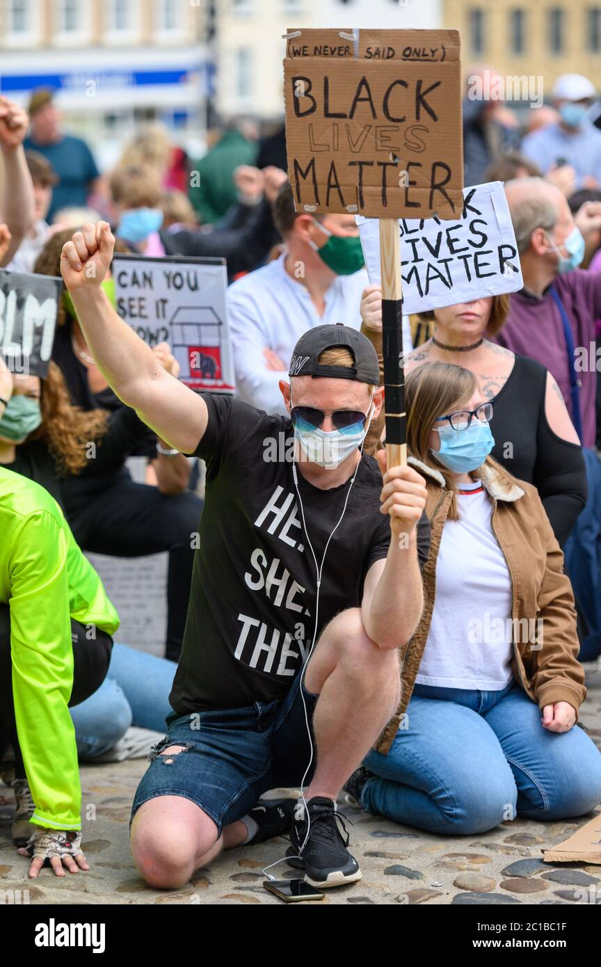 Richmond, North Yorkshire, Royaume-Uni - 14 juin 2020 : un manifestant porte un masque facial PPE tout en s'agenouillant sur des pavés, en salant et en tenant une matière noire Banque D'Images