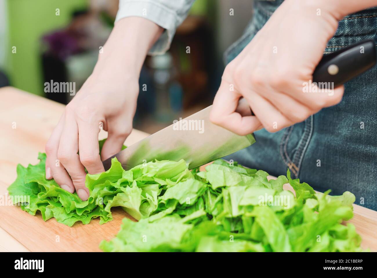 Gros plan les mains des femmes hachent une salade de plantes vertes cuisant de la salade de légumes sur une planche à découper en bois à la maison. Le concept Banque D'Images