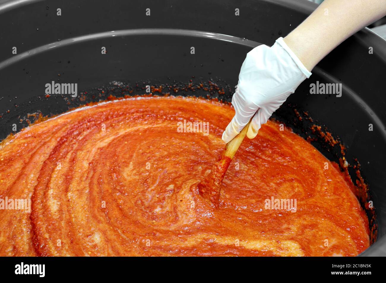La main droite portait des gants en caoutchouc, remuant dans la sauce à l'orange. Préparez-vous à la cuisine coréenne. Banque D'Images