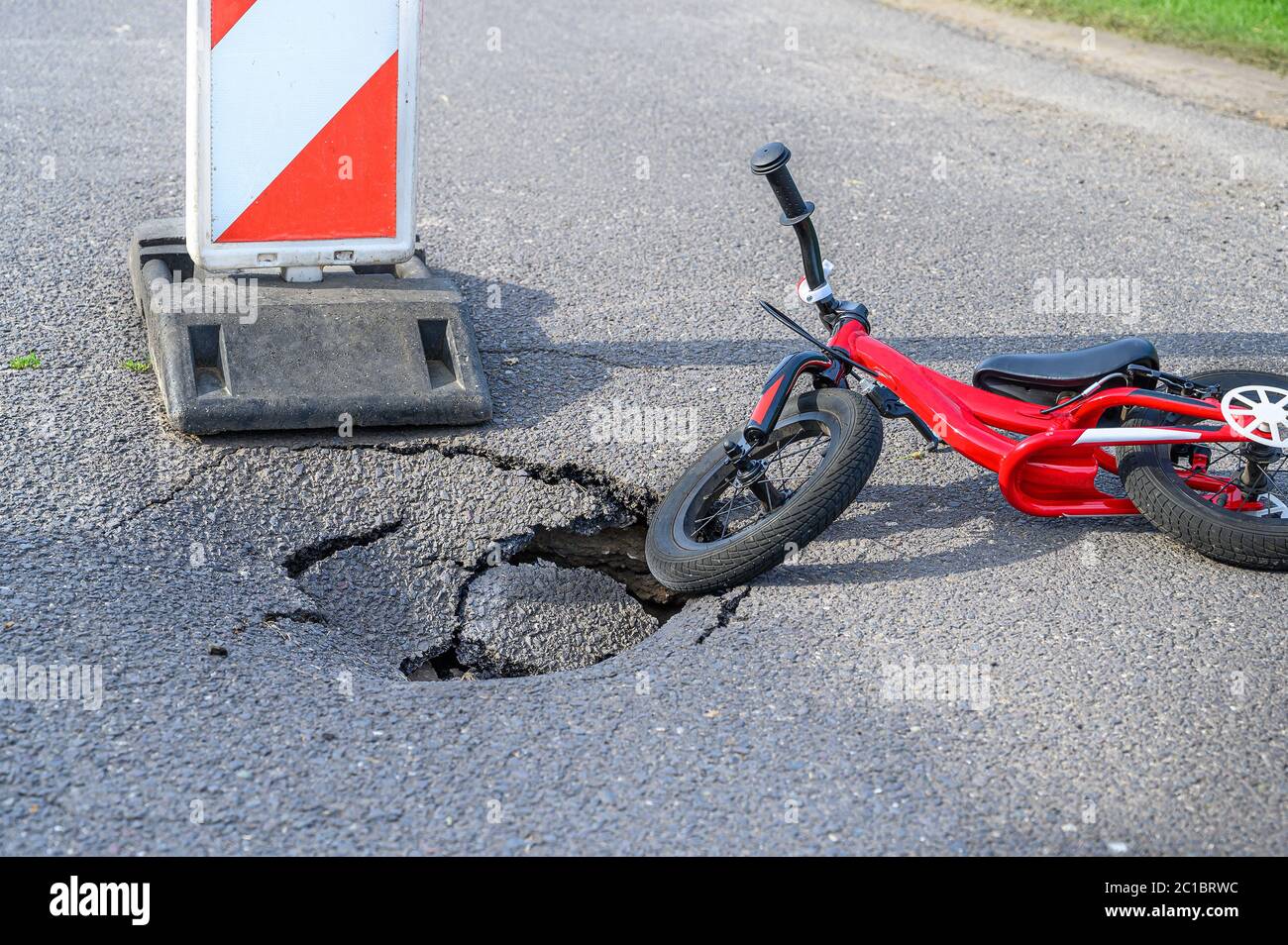 Equilibrer le vélo (pousser le vélo) à côté de la pothole sur la rue asphaltée avec le panneau de signalisation routière d'alerte de détour Banque D'Images