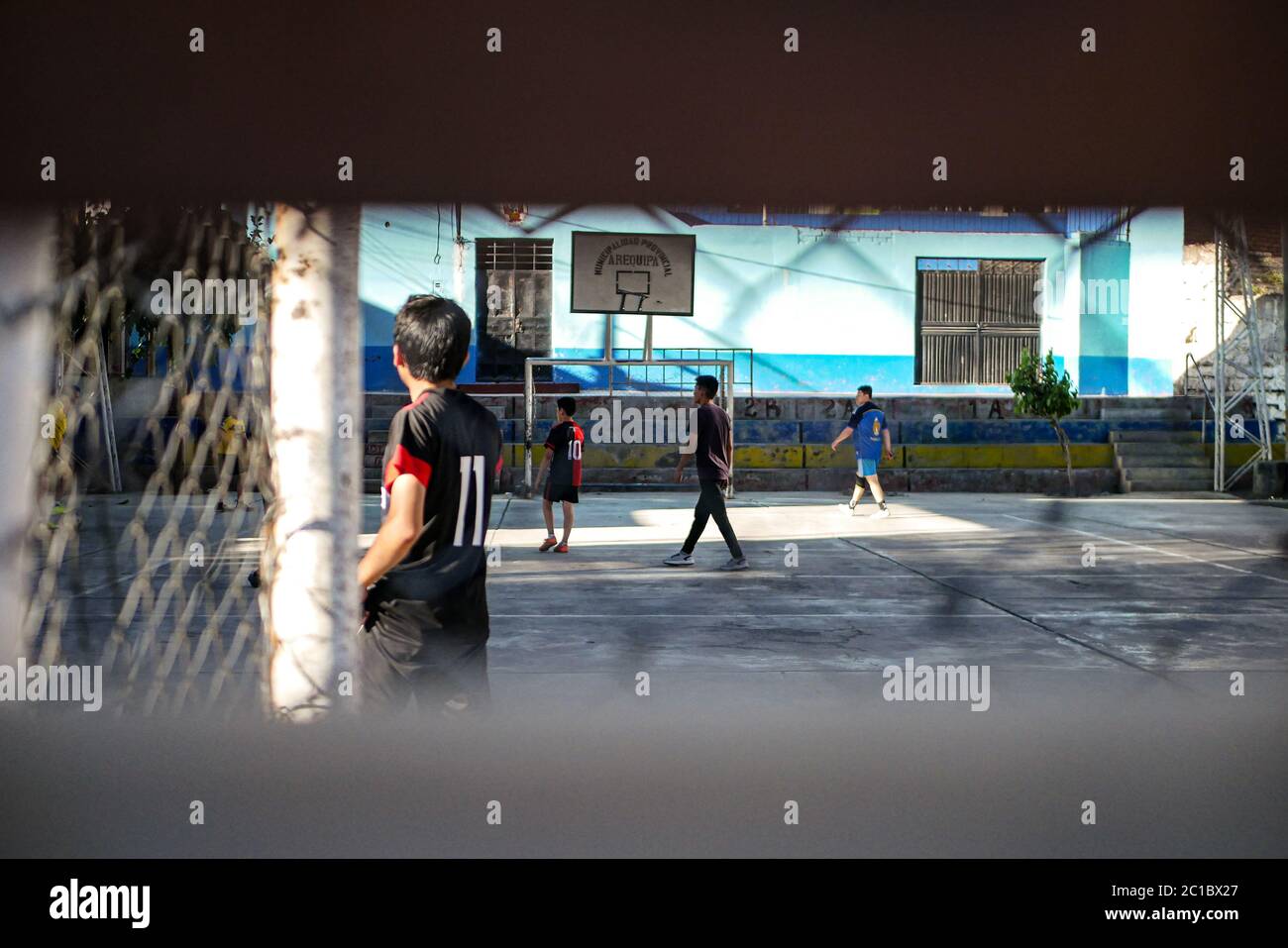 Vue sur le groupe de jeunes garçons jouant au football sur le terrain de jeu en béton du campus de l'école derrière la clôture. Banque D'Images