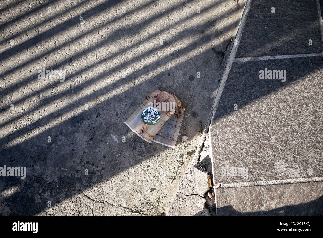 Une tasse en plastique de café piétiné de la célèbre marque sur un sol en béton avec les lignes d'ombre dessus pendant le coucher du soleil. Banque D'Images