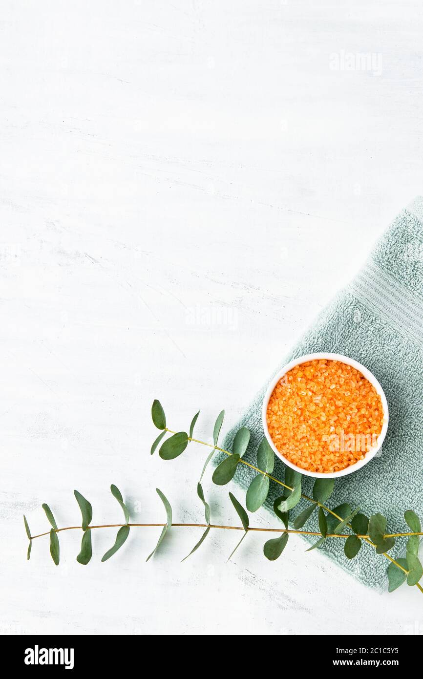 Serviette verte roulée, sel de bain orange et branche d'eucalyptus vert sur fond blanc. Hygiène, bien-être, concept de soins du corps. Copier l'espace, haut Banque D'Images