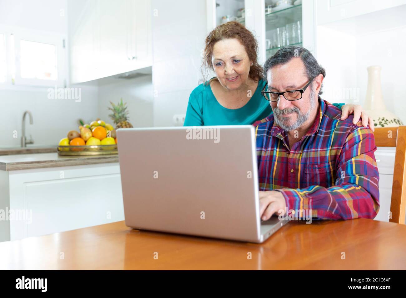 Un couple de personnes âgées souriantes utilisant un ordinateur portable à la maison. Adaptation à la technologie des personnes âgées concept. Banque D'Images