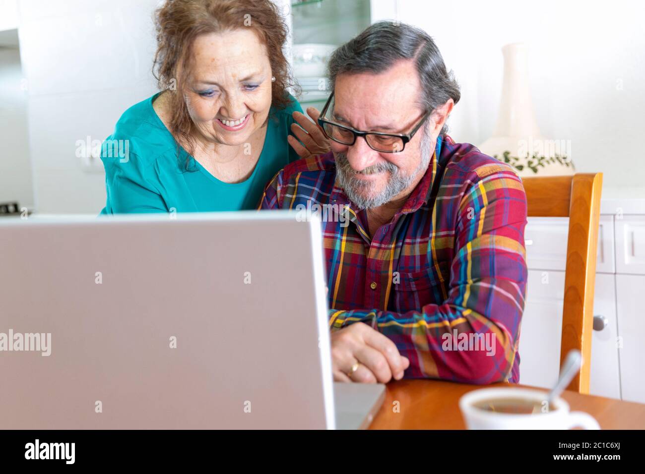 Un couple plus âgé souriant à la maison devant l'écran de son ordinateur portable. Restez à la maison et nouveau concept de communication. Banque D'Images