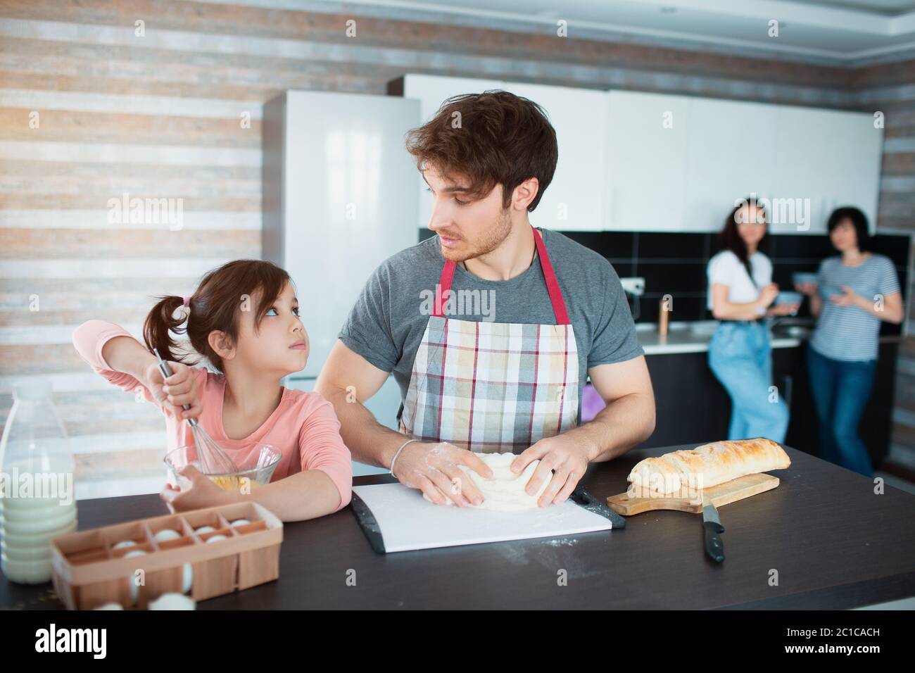 Une famille heureuse cuisine dans la cuisine. Père enseigne à la fille de couper des légumes. Mère et grand-mère se tiennent en arrière-plan. Ils s'agenouillent le doug Banque D'Images
