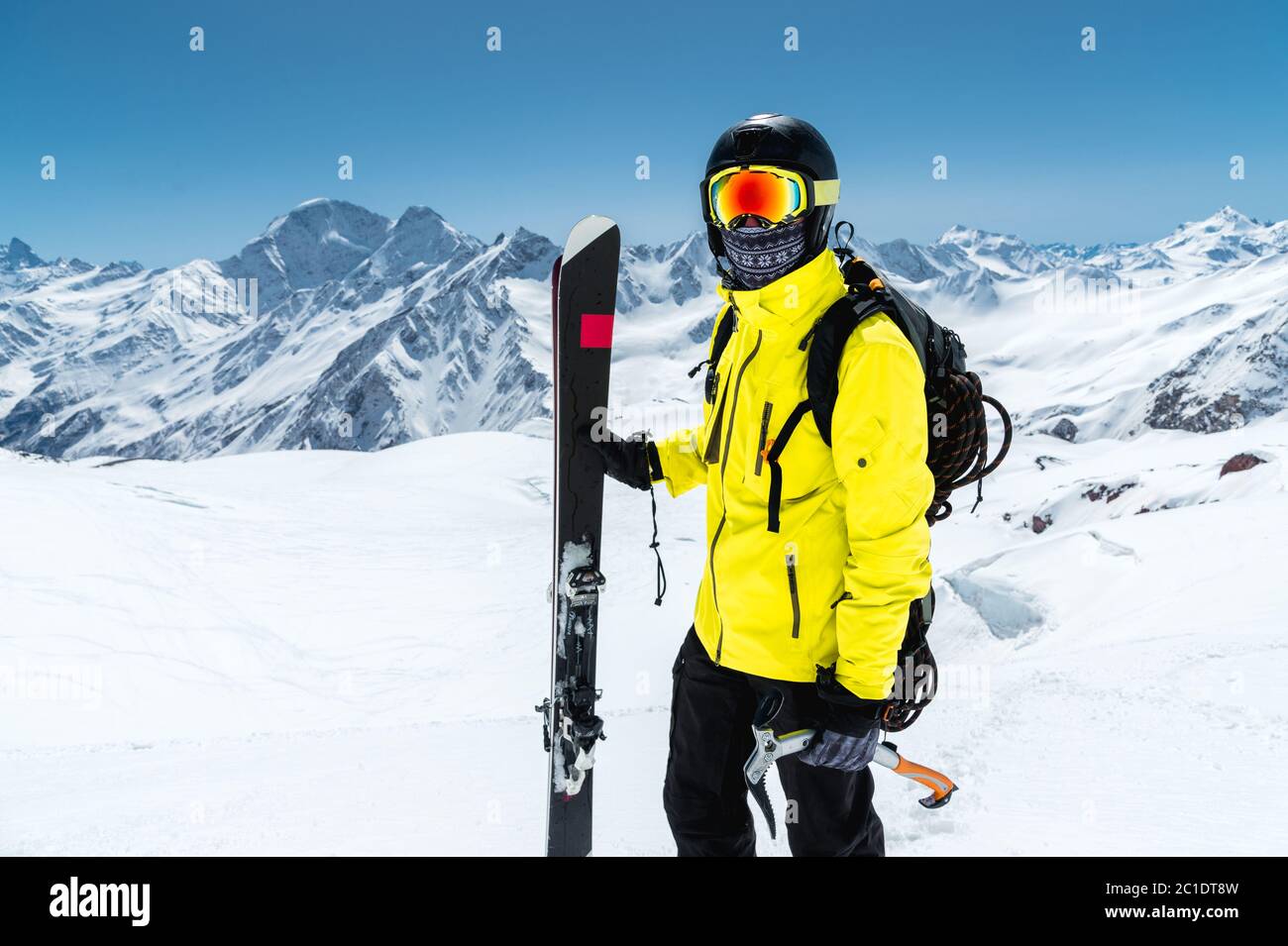 Portrait en gros plan d'un skieur portant un casque et des lunettes de protection. Un masque et une écharpe avec une hache de glace dans ses mains à côté des skis Banque D'Images