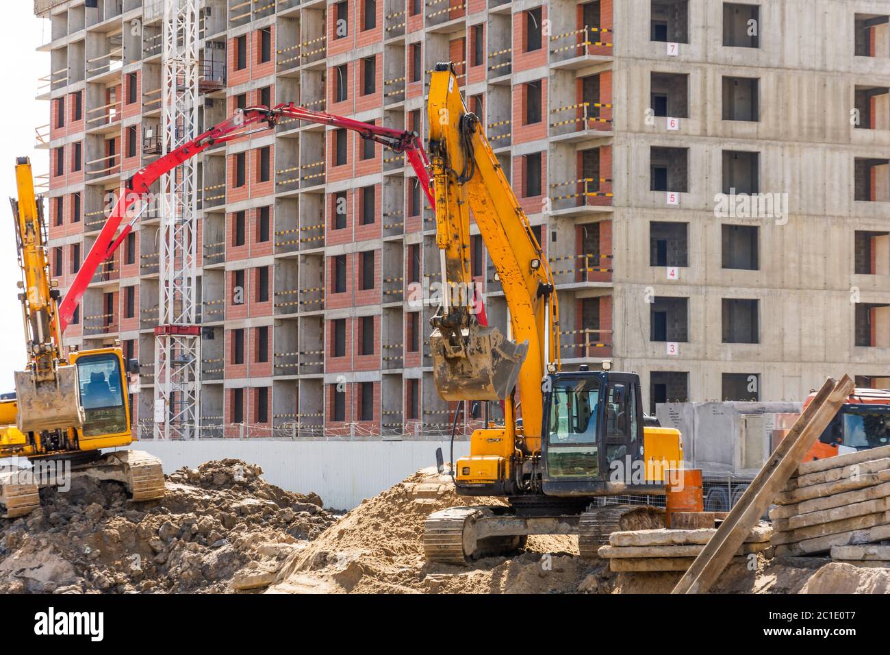Pelles hydrauliques avec godets surélevés sur le fond d'un bâtiment résidentiel de plusieurs étages en construction Banque D'Images