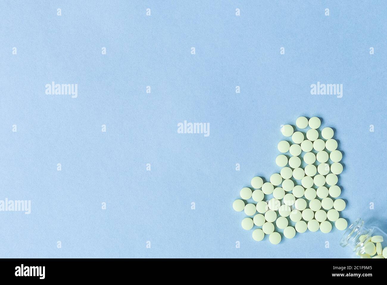 Les comprimés ronds jaunes sont en forme de coeur versé dans une bouteille de verre sur fond bleu pastel. Concept de soins de santé, de traitement et de preve Banque D'Images