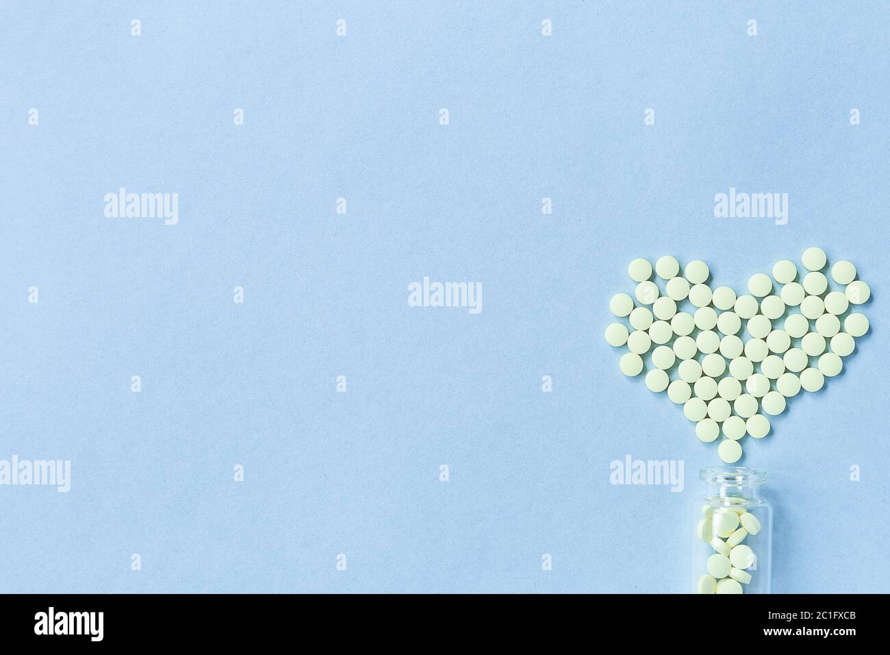 Un groupe de comprimés ronds jaunes forme un coeur sur fond bleu, déversé d'un pot en verre. Concept de soins de santé, de traitement et de prévention o Banque D'Images