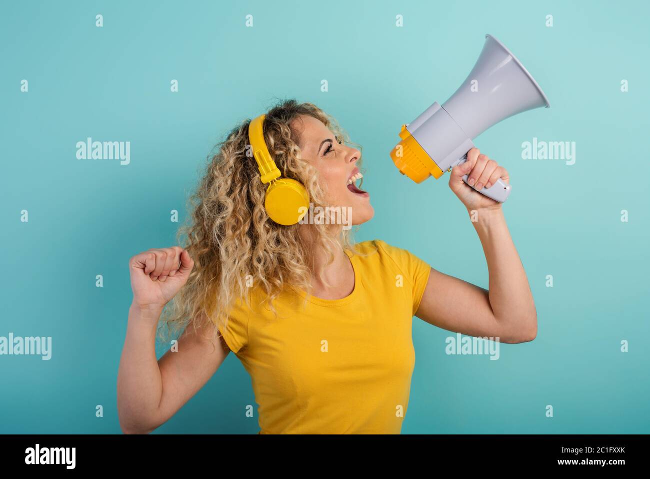 Femme chante avec haut-parleur et écoute de la musique avec casque. Expression joyeuse. Fond cyan Banque D'Images