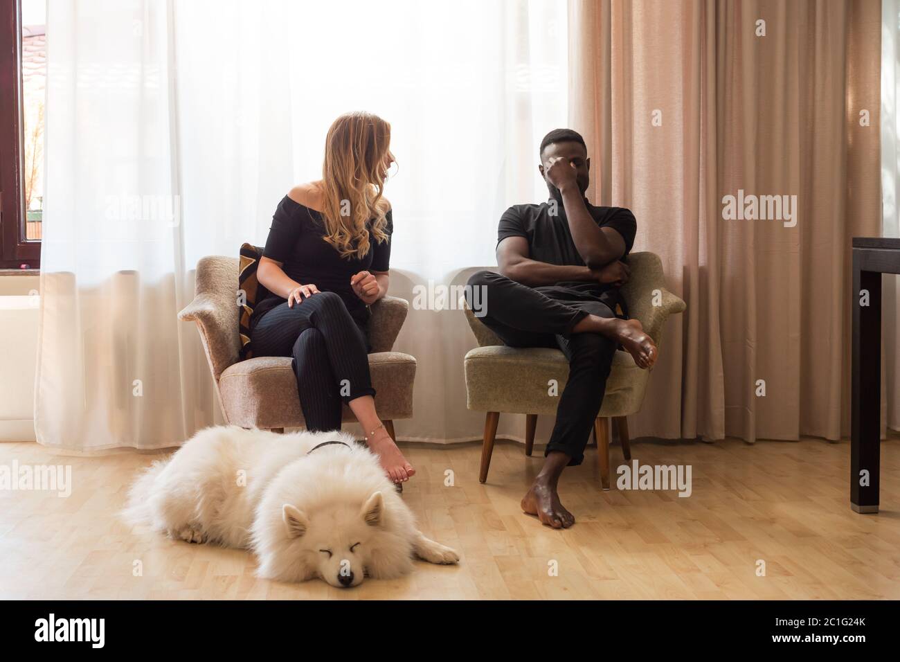 Homme et femme assis dans les fauteuils du salon avec un chien devant. Banque D'Images