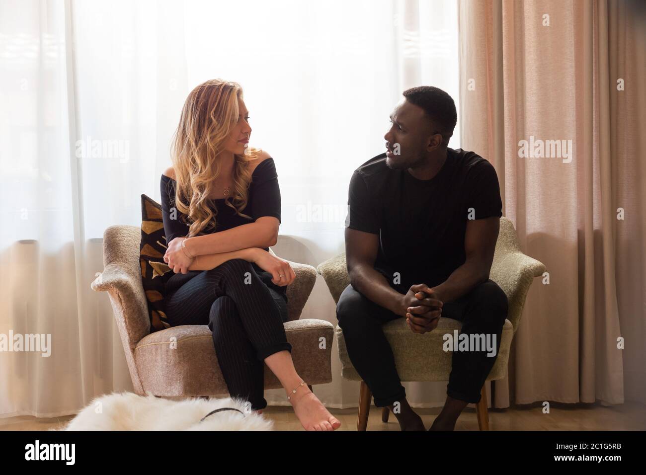 Portrait d'un couple de race mixte assis dans des fauteuils séparés parlant. Longueur totale. Banque D'Images