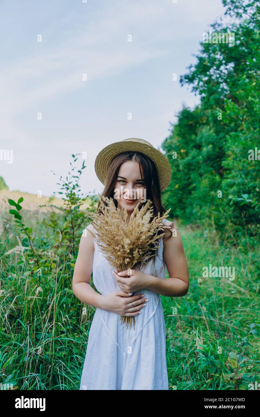 Belle fille dans une robe blanche avec un bouquet de fleurs séchées. Jeune femme dans un parc vert. Fille dans une robe et un jour ensoleillé d'été Banque D'Images