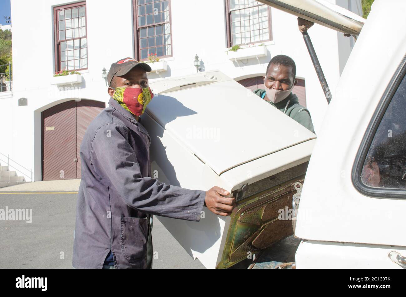 Deux hommes de travail chargent un lave-vaisselle dans une voiture, tous deux portant des masques conformément à la loi sud-africaine Covid 19 Banque D'Images
