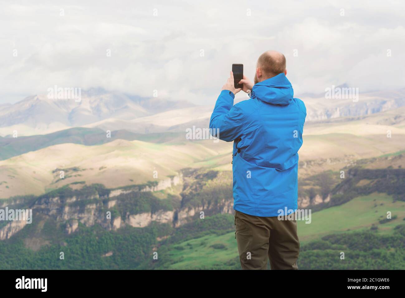 Un homme barbu dans une veste bleue à membrane se dresse dans la nature sur fond de montagnes et prend des photos sur le téléphone Banque D'Images