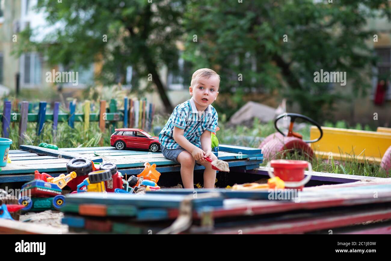 Un enfant joue dans l'aire de jeux avec des jouets dans le bac à sable. Un tout petit garçon joue dans le sable en été. Vacances pour enfants à l'extérieur. Banque D'Images