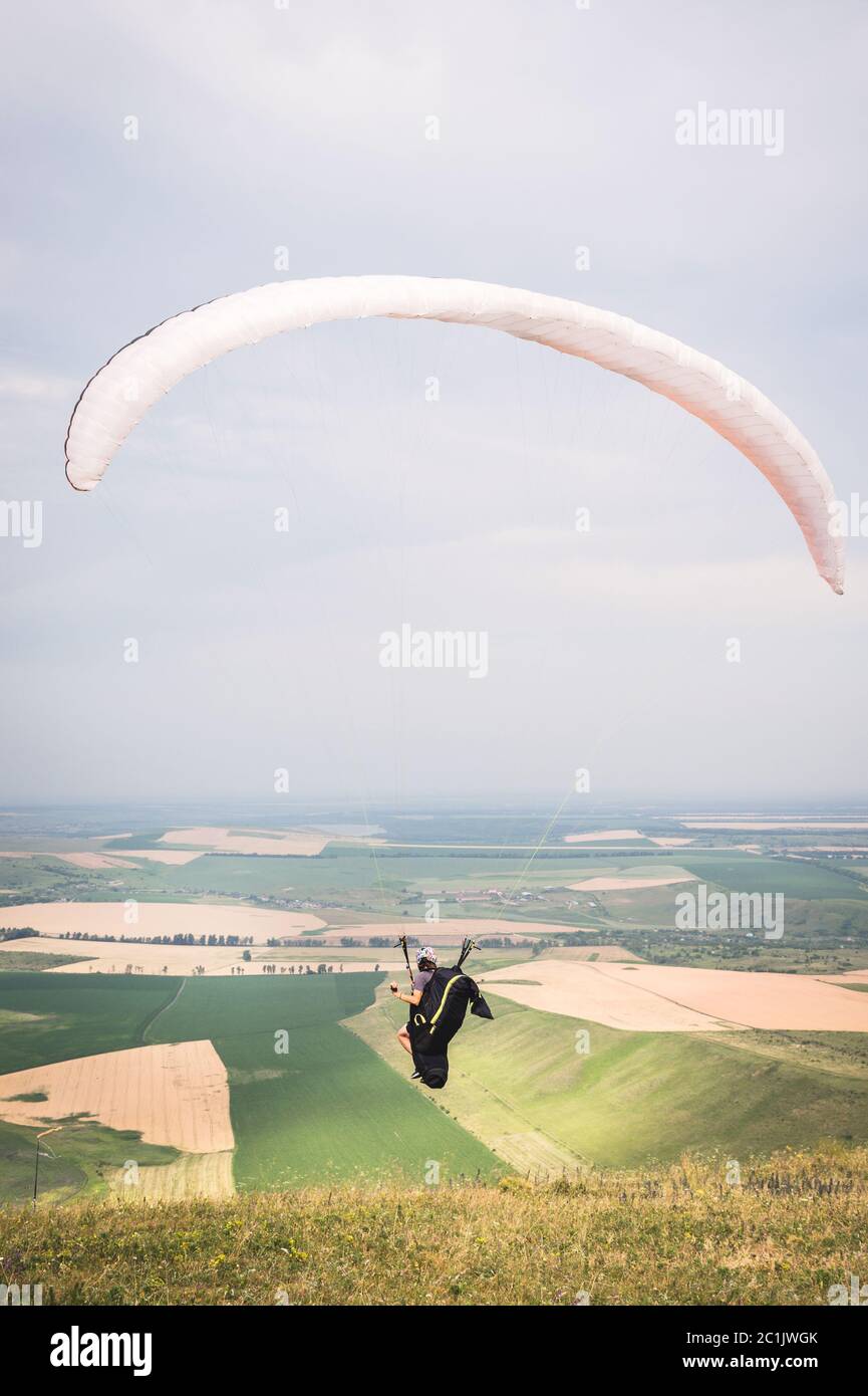 Un parapente d'homme qui s'enchaîne du bord de la montagne avec des champs en arrière-plan. Parapente Banque D'Images