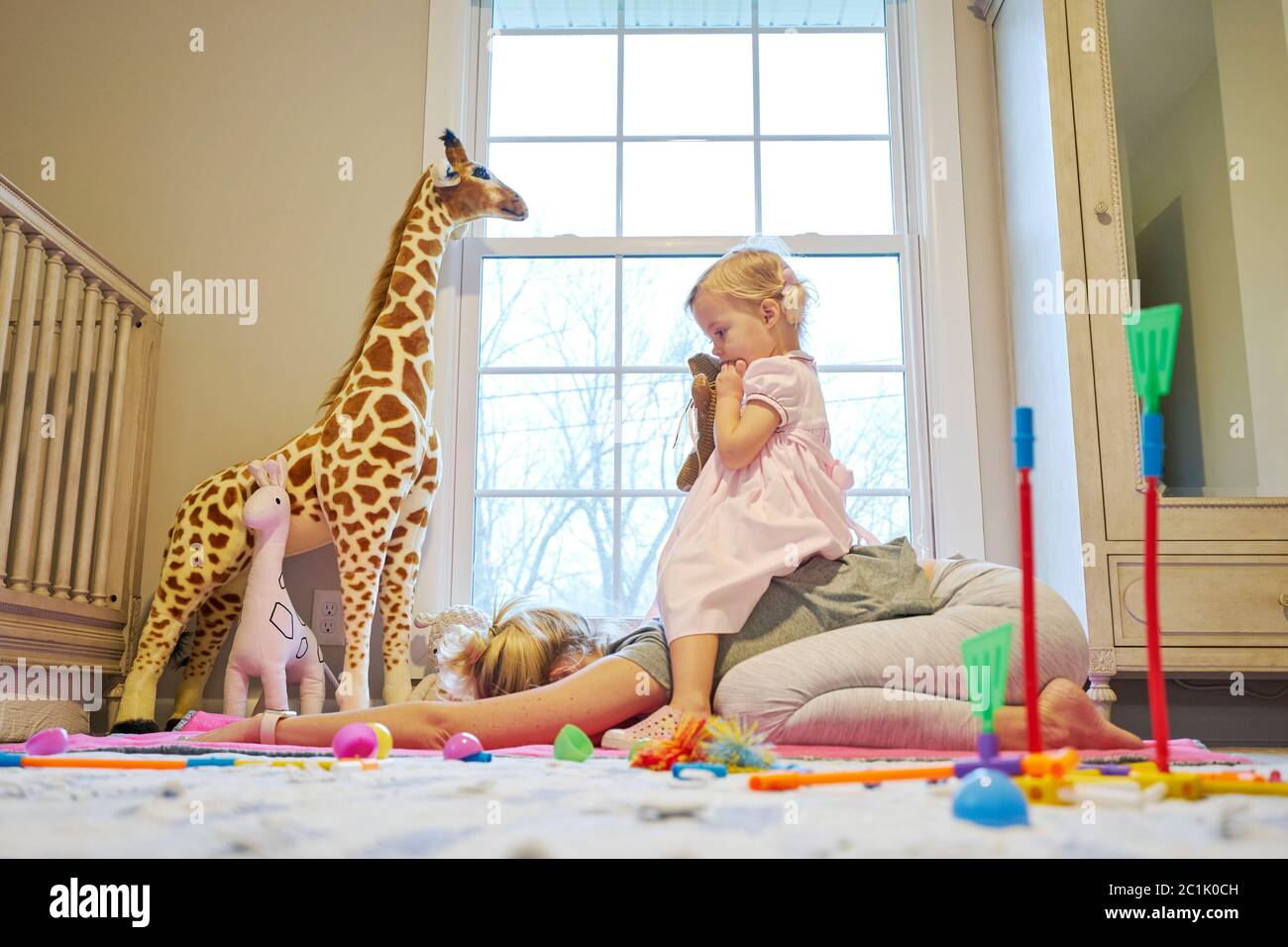 La petite fille s'assoit sur le dos de sa maman comme elle le fait pose de l'enfant de yoga Banque D'Images