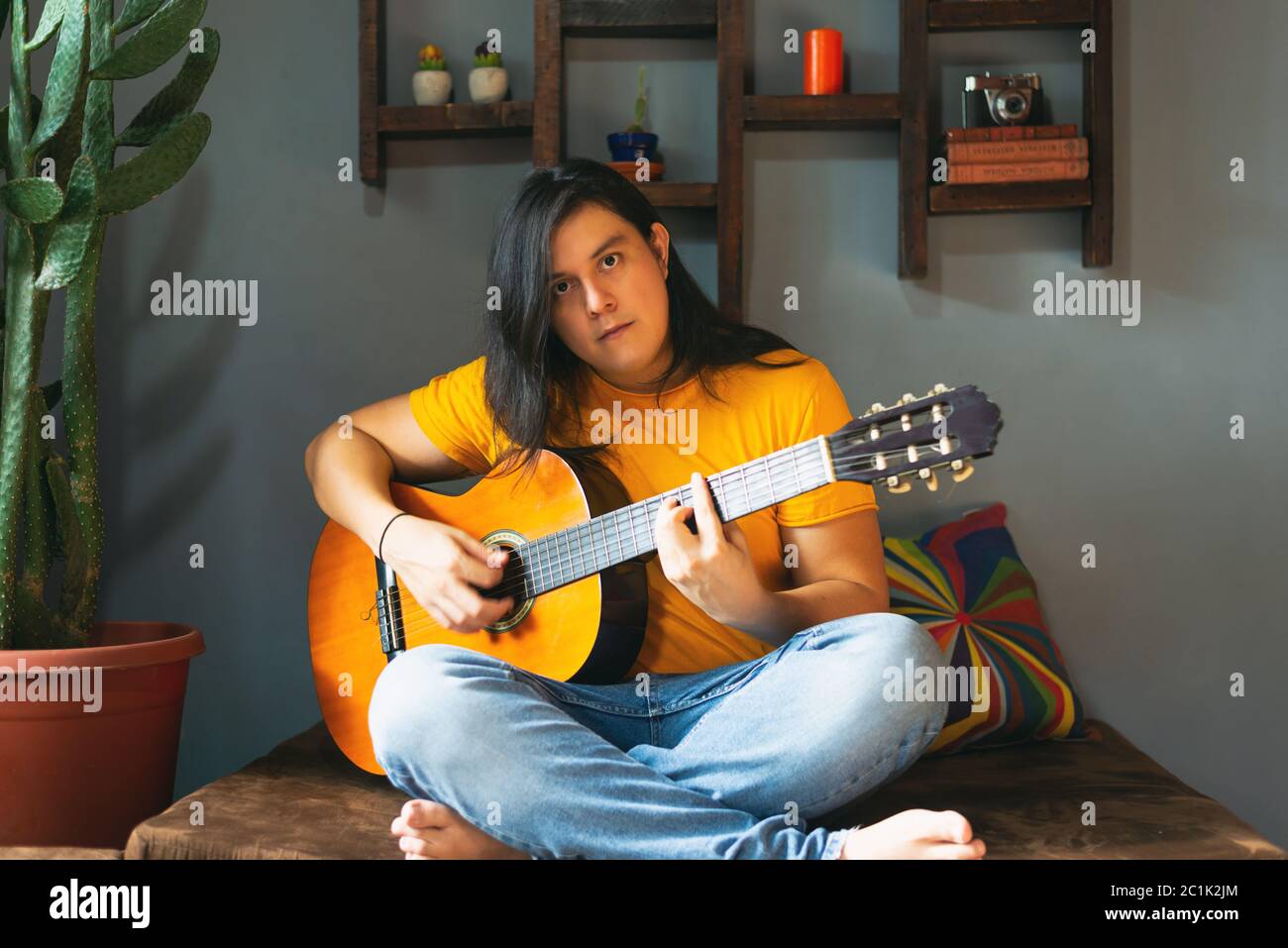 homme aux cheveux longs jouant de la guitare acoustique à la maison pendant quarantaine Banque D'Images