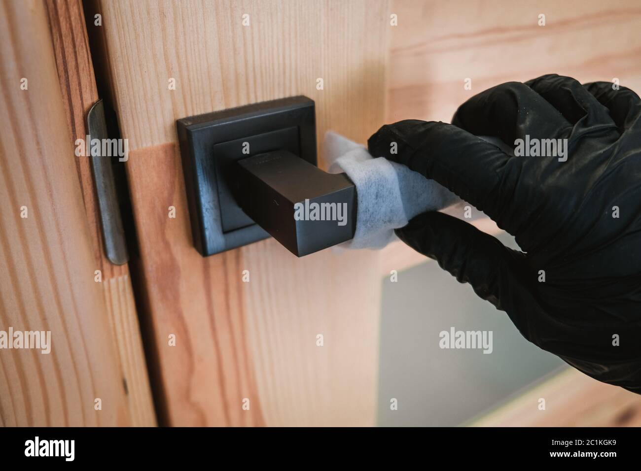 Ouverture d'une porte en bois avec des gants noirs à l'aide d'une serviette. Auto-protection lors de l'isolement des épidémies virales. Mesures de sécurité personnelle pour prévenir les virus Banque D'Images