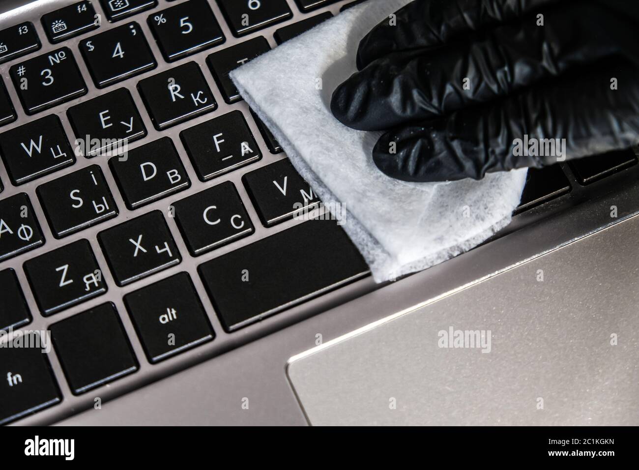 Nettoyage du clavier de l'ordinateur portable avec des lingettes humides antibactériennes. Gant noir et serviette blanche sur un ordinateur noir. Éliminer la poussière et tuer les bactéries Banque D'Images