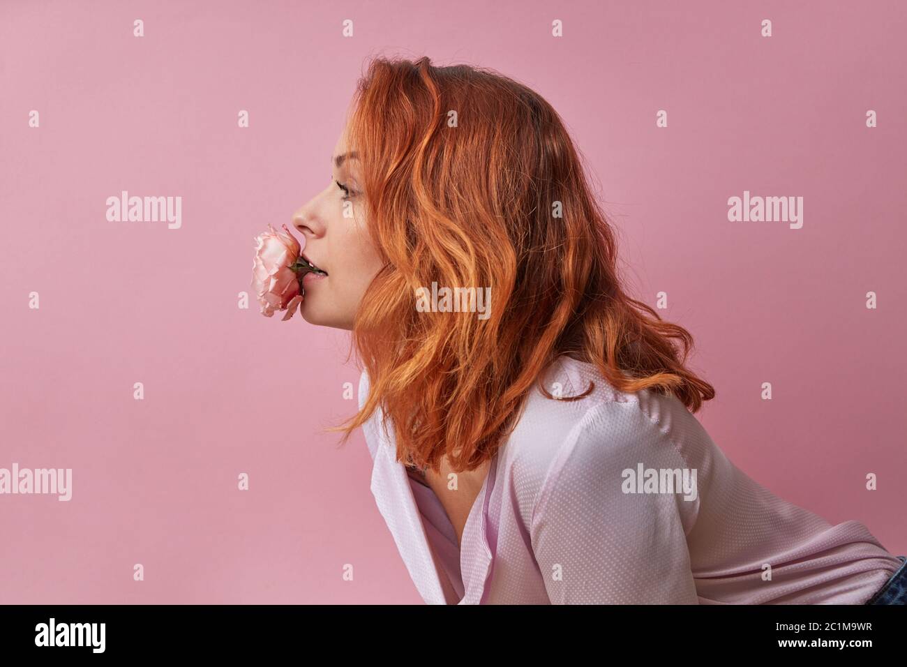 Studio photo de mode de belle jeune femme avec des fleurs dans sa bouche isolée sur rose Banque D'Images