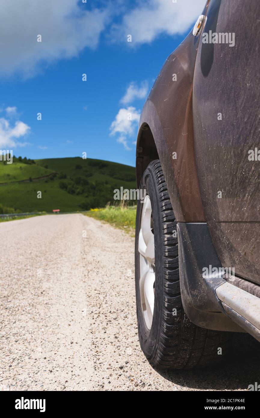 Gros plan d'une roue de SUV sur une route asphaltée à l'extérieur de la ville contre les collines verdoyantes du ciel bleu et des nuages Banque D'Images