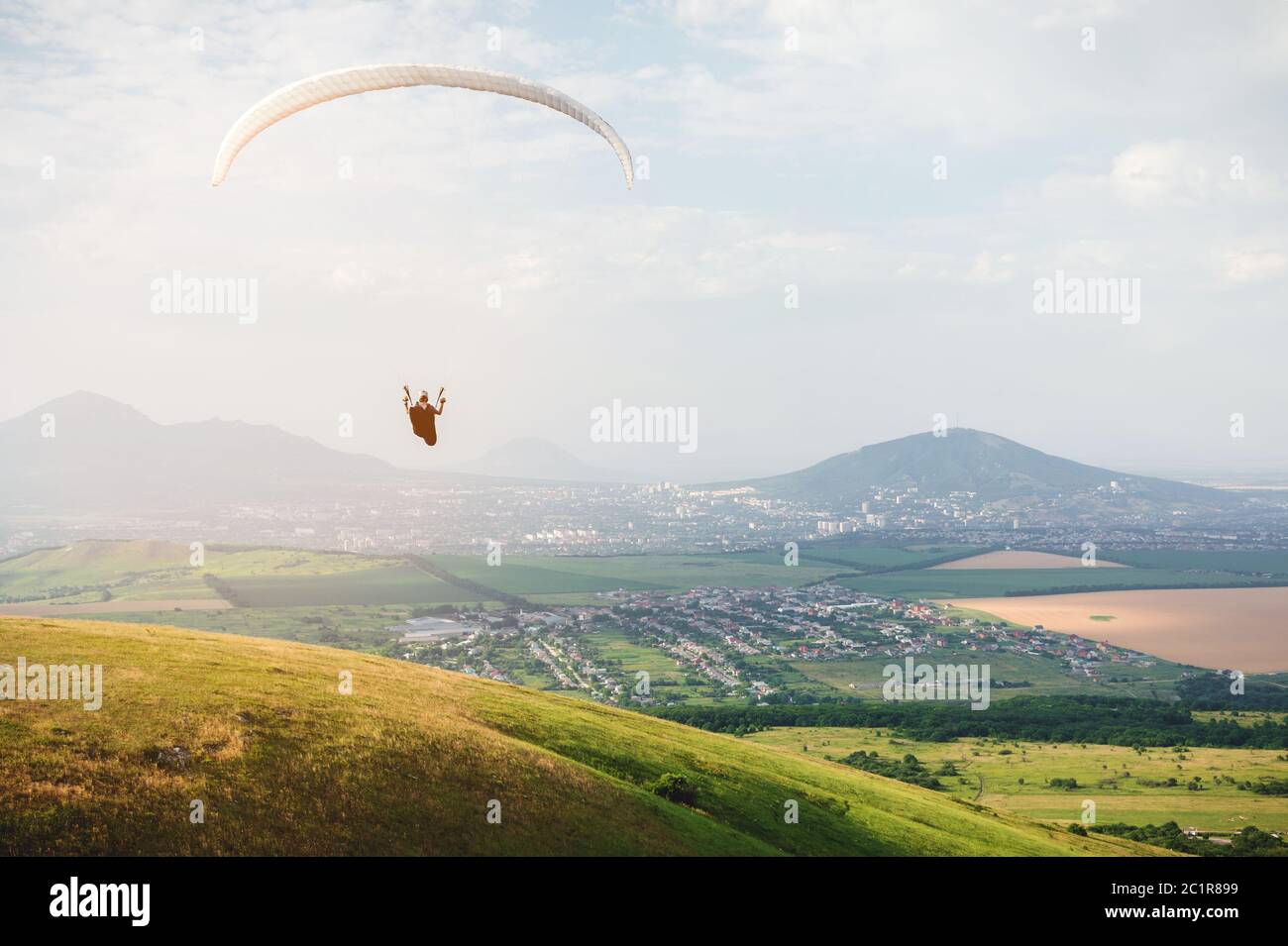 Un parapente professionnel dans un cocon suit des mouches au-dessus du sol contre le ciel et les champs avec des montagnes Banque D'Images