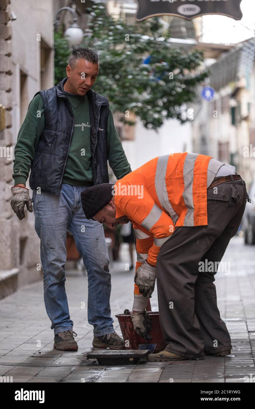 Deux travailleurs ouvrent un trou d'égout non sécurisé dans une rue de la ville d'Ascoli Picena, en Italie Banque D'Images