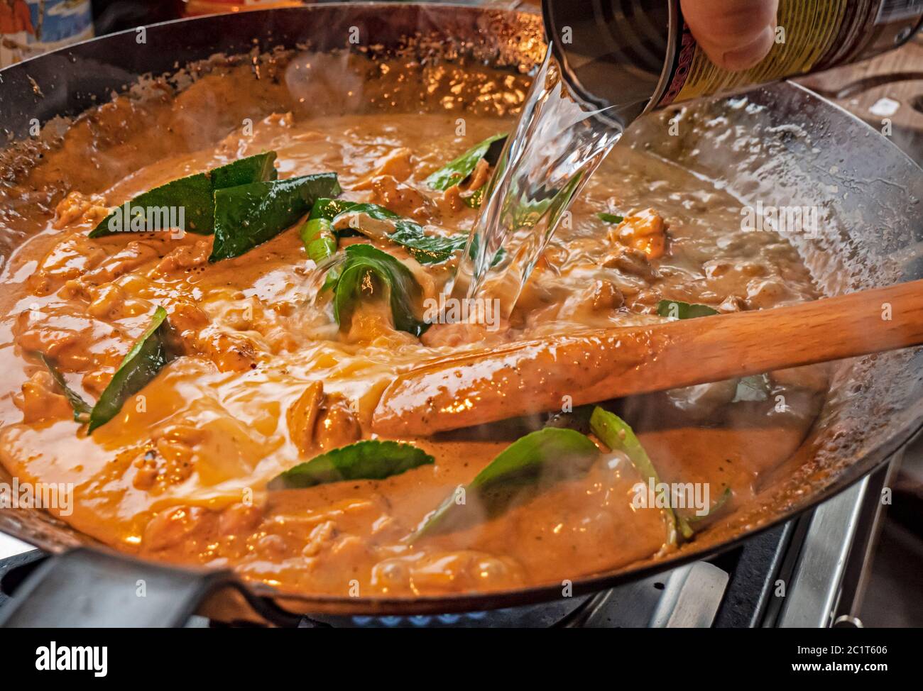 L'eau est ajoutée à un wok pour préparer la sauce crémeuse d'un curry de  poulet rouge thaïlandais. La sauce crémeuse à la noix de coco cuit les  légumes et la viande dans