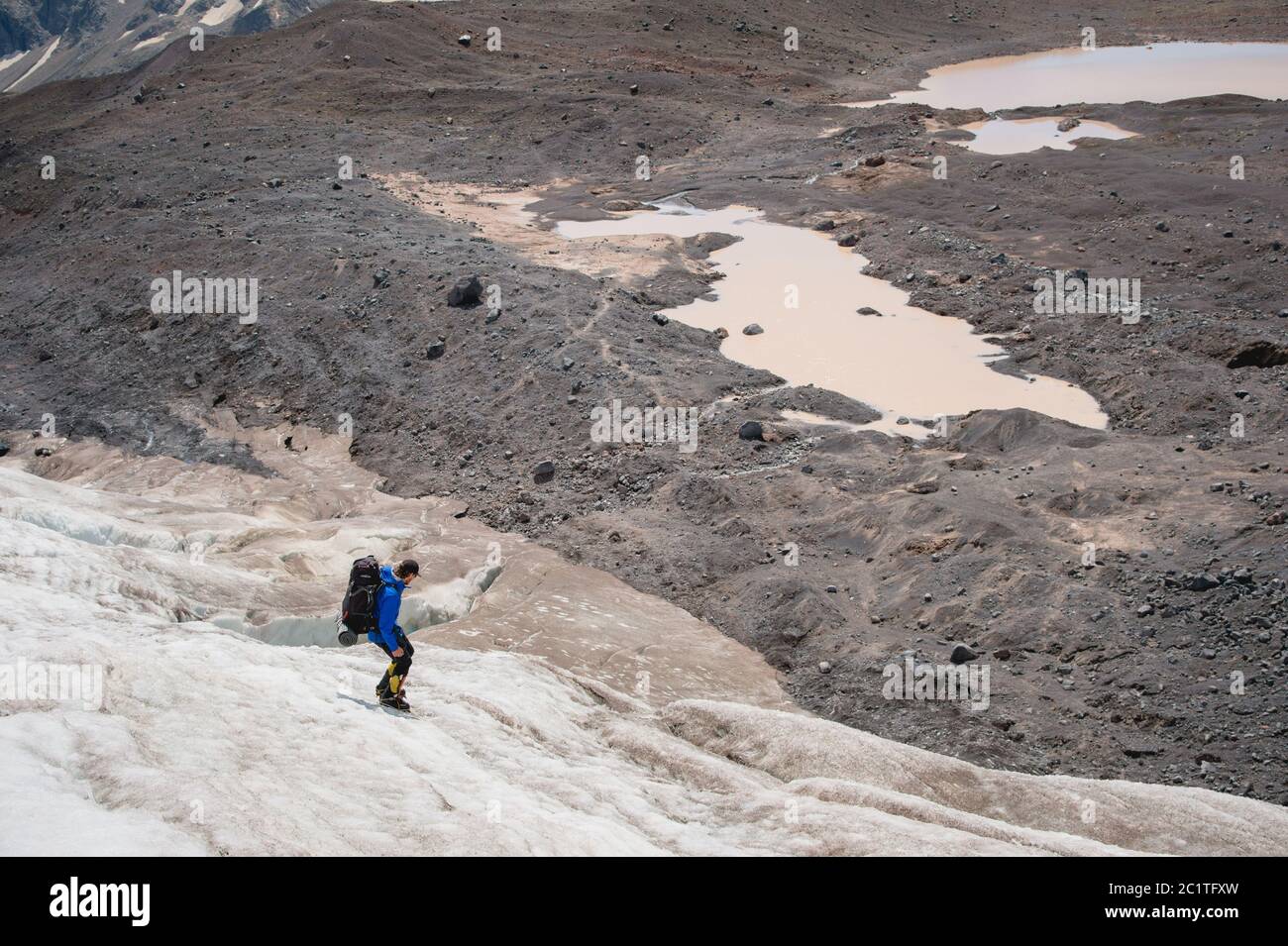 Un alpiniste avec un sac à dos marche dans des crampons le long d'un glacier poussiéreux avec des trottoirs dans les mains entre les fissures dans le Banque D'Images
