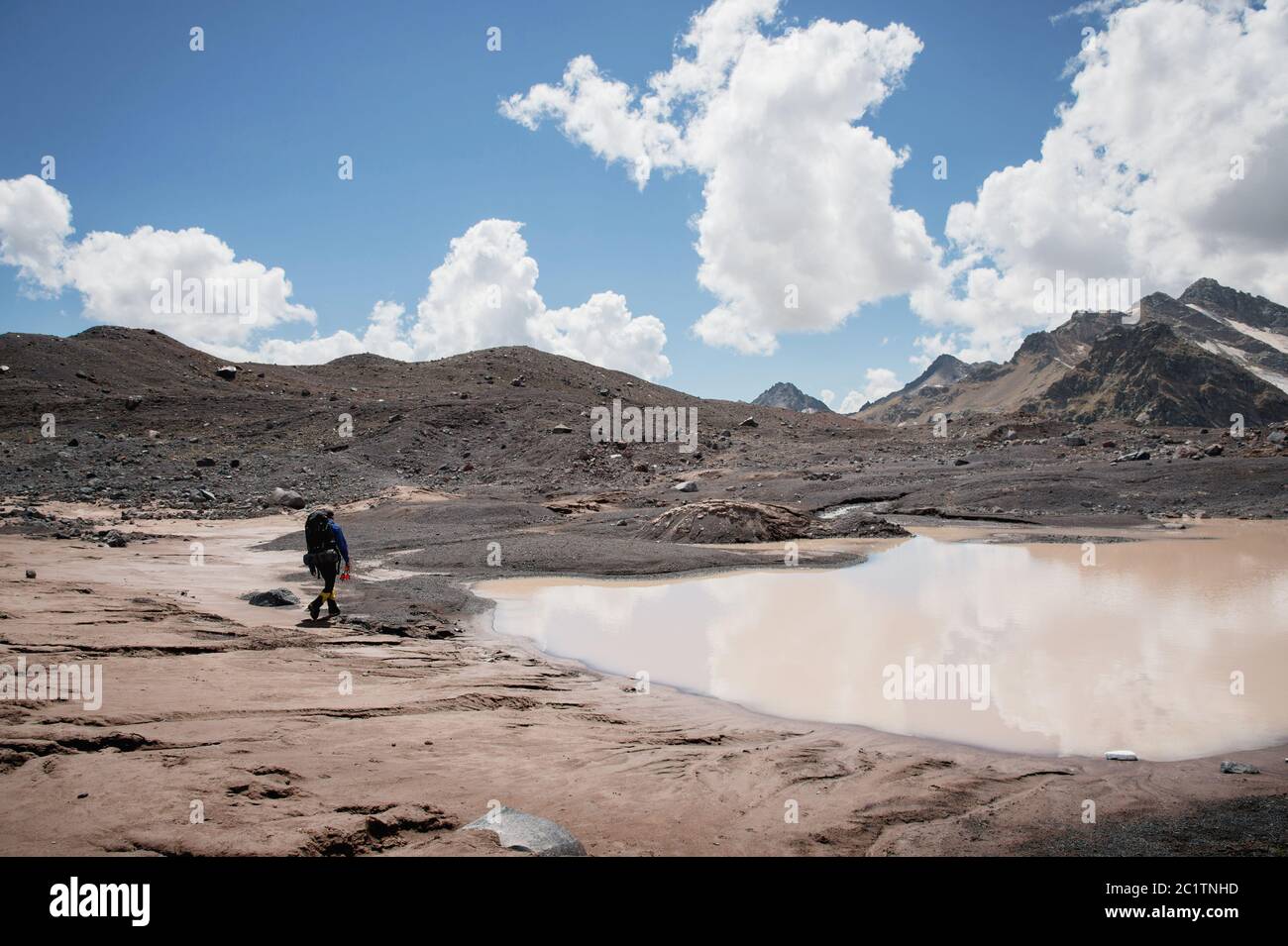 Un alpiniste avec un sac à dos marche dans des crampons le long d'un glacier poussiéreux avec des trottoirs dans les mains entre les fissures dans le Banque D'Images