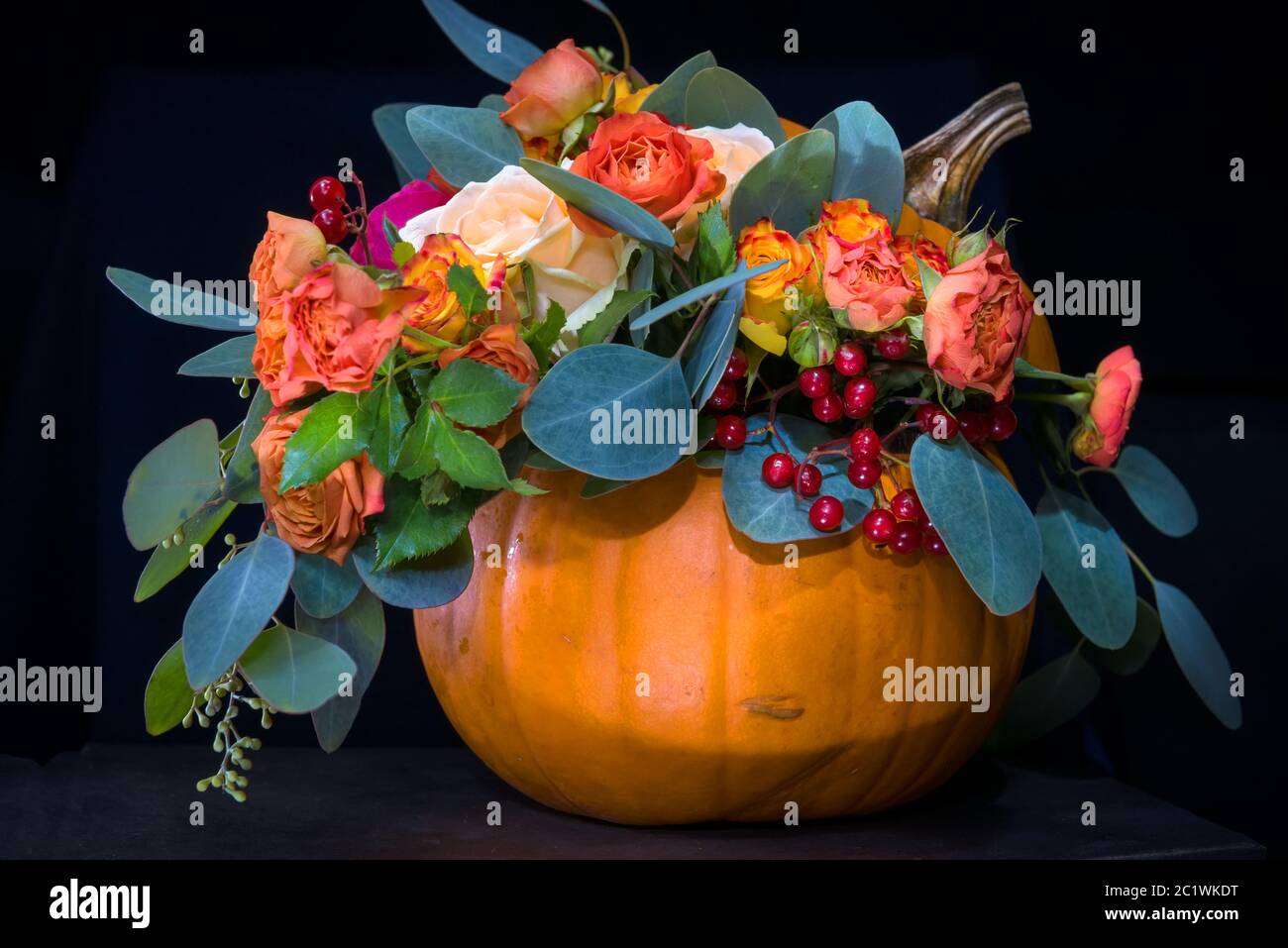Bouquet de fleurs dans une citrouille comme dans un vase sur fond noir Banque D'Images