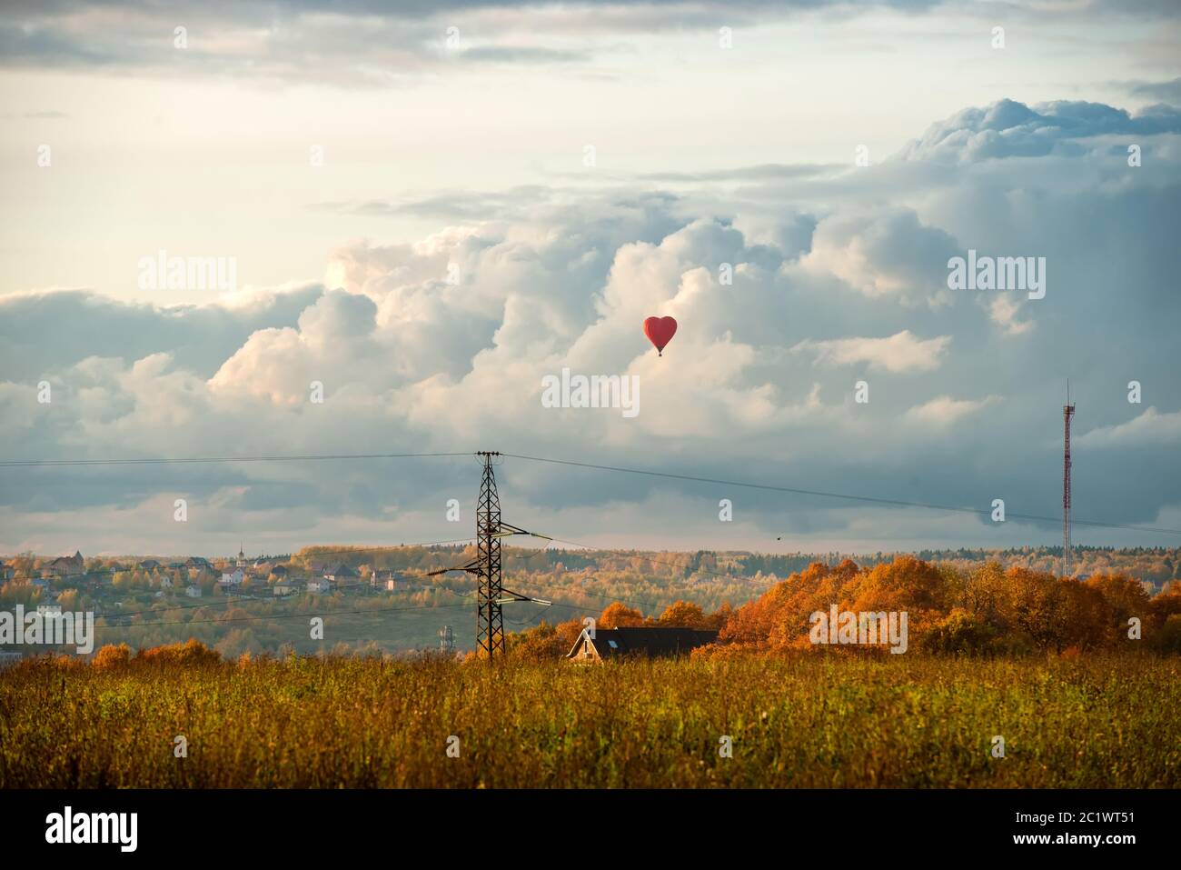 Ballon coloré en forme de coeur d'air chaud volant contre le ciel nuageux dans la campagne, le soir d'automne Banque D'Images